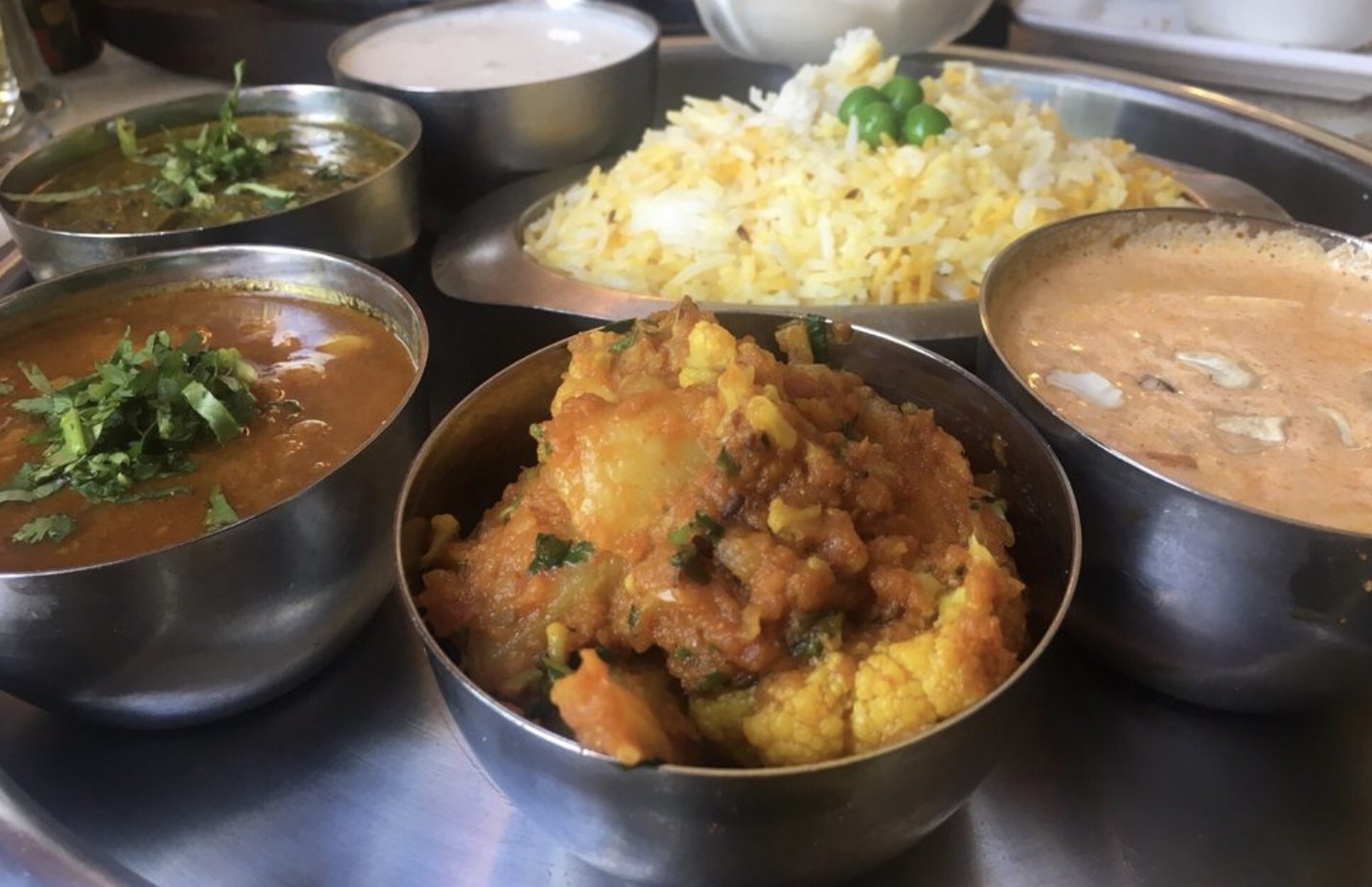 Assorted Indian curries, saffron rice, and raita served in steel catering bowls